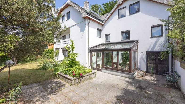Rückseite des Hauses mit gepflasterter Terrasse und einem verglasten Wintergarten.