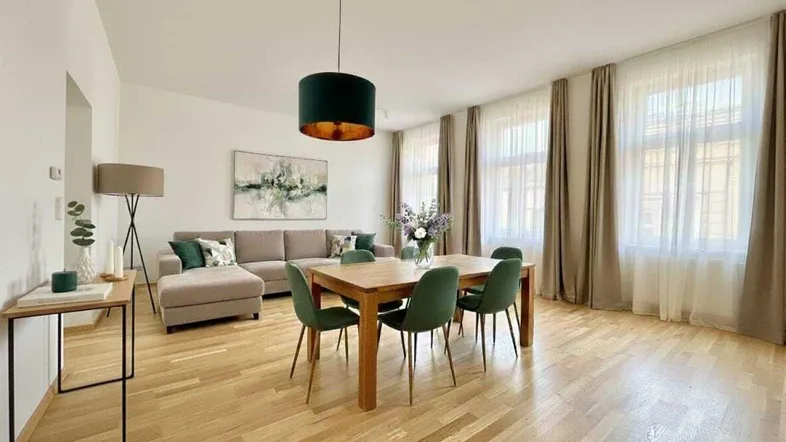 Helles, modern eingerichtetes Wohn-Esszimmer mit Holzboden, beiger Couch und grünem Esstisch.