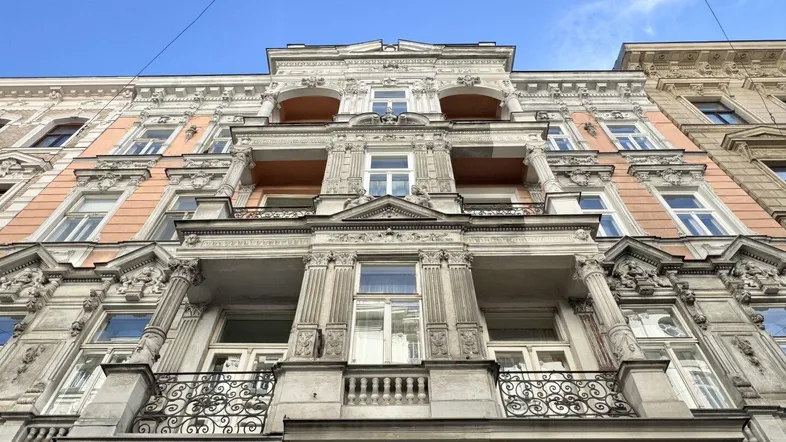 Prächtige Altbaufassade mit reich verzierten Balkonen und architektonischen Details unter blauem Himmel.