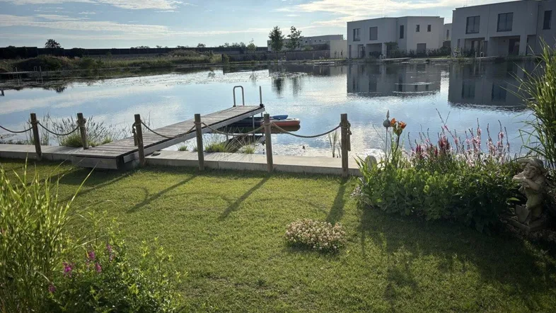 Gepflegter Garten mit direktem Zugang zu einem See und Blick auf moderne Häuser.