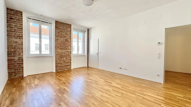 Helles Zimmer mit freigelegten Ziegelwänden und Parkettboden, ideal als Wohn- oder Schlafbereich.