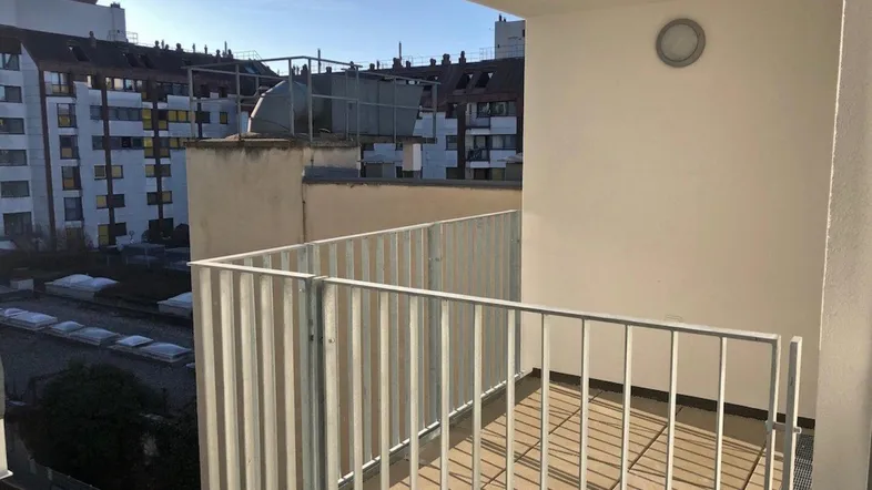 Heller Balkon mit Metallgeländer und Blick auf umliegende Gebäude in der Stadt.