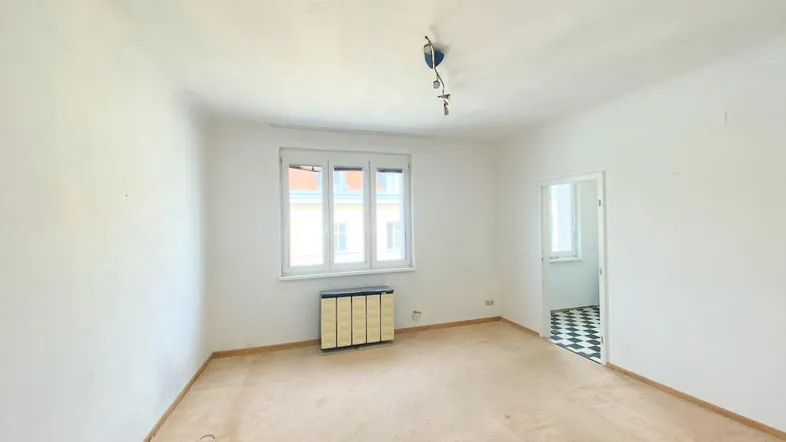 Geräumiges Wohnzimmer mit Teppichboden, einem Fenster und einem Heizkörper.
