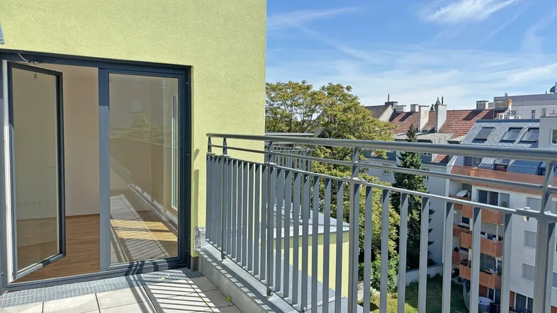 Geräumiger Balkon mit Metallgeländer und Blick auf die umliegende Stadtlandschaft und Bäume.