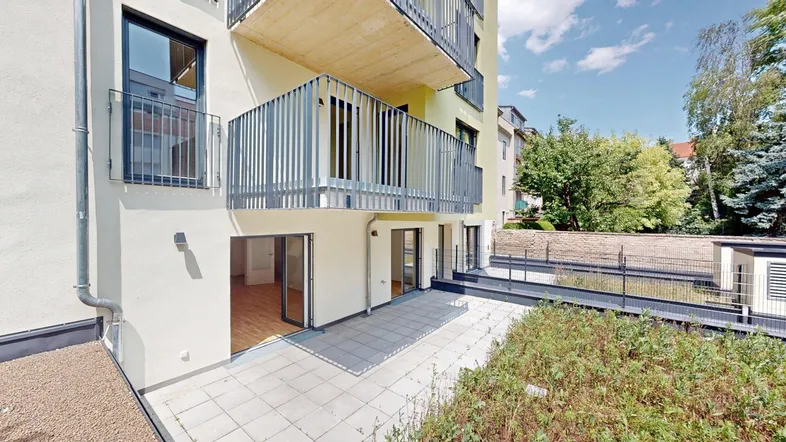 Blick auf die moderne Gebäudefassade mit Balkonen und einer großzügigen, gefliesten Terrasse im Erdgeschoss.