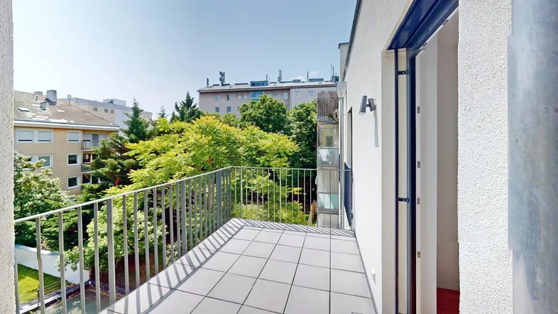 Geräumiger Balkon mit Fliesenboden und Blick auf die umliegenden Gebäude und Bäume.