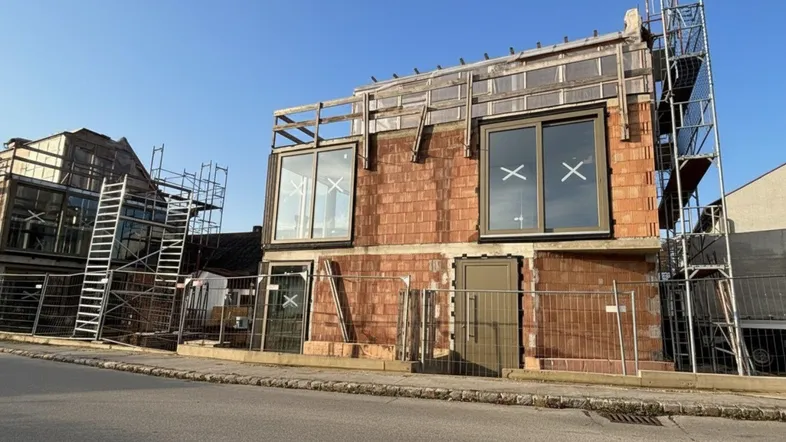 Neubau im Rohbauzustand mit großen Fenstern, Gerüst und massiver Bauweise.