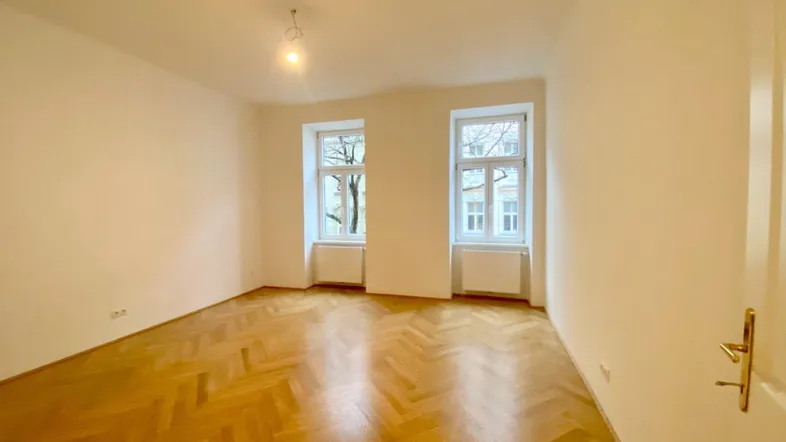 Heller Raum mit Fischgrätparkettboden und zwei Fenstern, ideal als Wohn- oder Schlafzimmer.