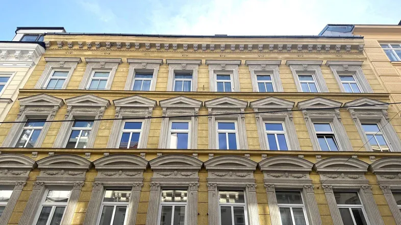 Historische Fassade eines Altbaus mit vielen Fenstern und dekorativen Elementen unter blauem Himmel.