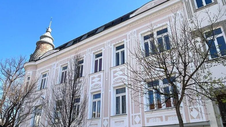 Historische Fassade eines Altbaus mit vielen Fenstern und dekorativen Elementen unter blauem Himmel.