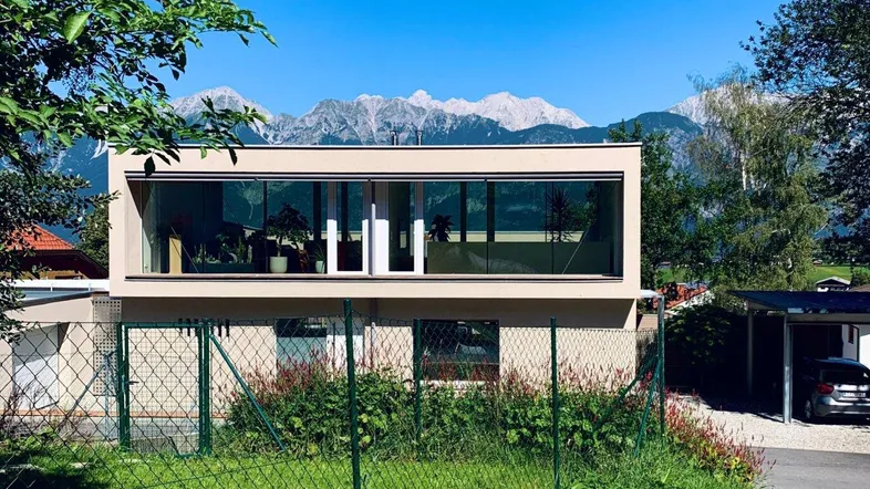 Moderne Architektur mit großen Glasfronten und beeindruckendem Bergblick im Hintergrund.