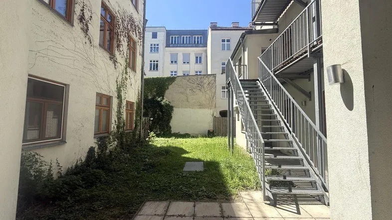 Innenhof mit Grünfläche, gepflastertem Bereich und Außentreppe zwischen den Gebäuden.