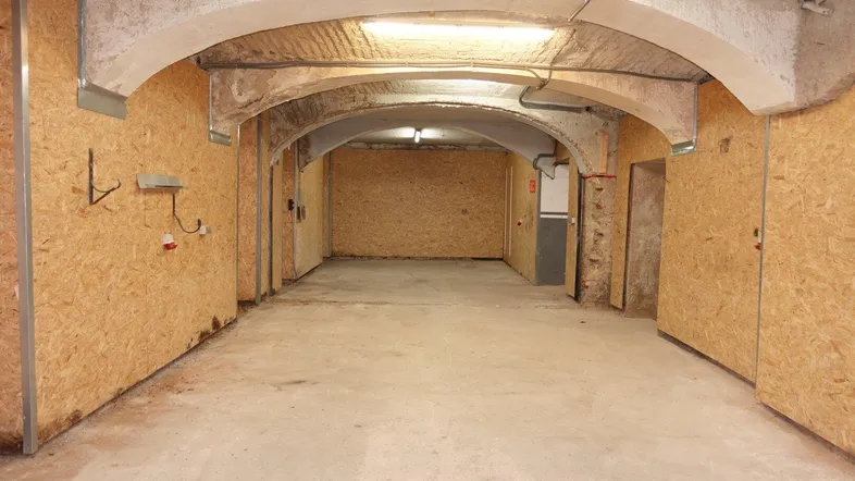 Großer Kellerraum mit gewölbter Betondecke und Wänden aus Holzspanplatten, bereit für den Ausbau.