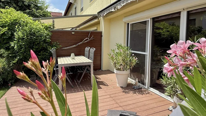 Detailansicht der Holzterrasse mit Gartenmöbeln und blühenden Pflanzen.