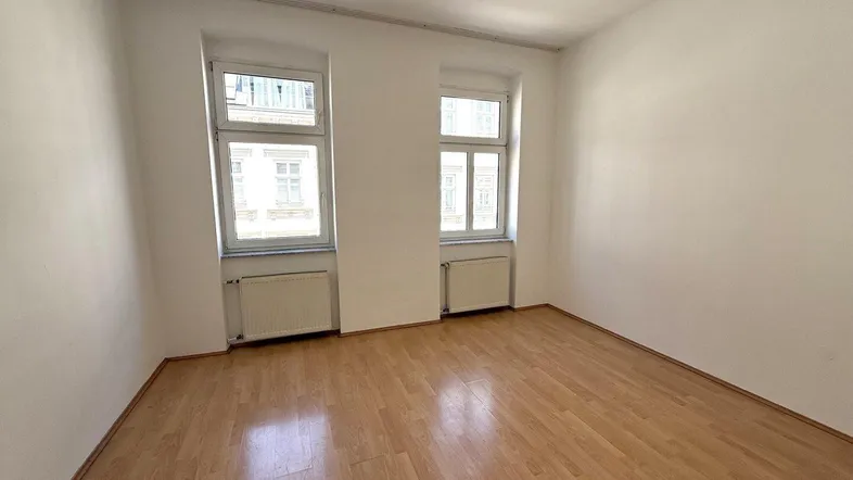 Helles Zimmer mit Holzfußboden und zwei Fenstern, ideal als Wohn- oder Schlafzimmer.