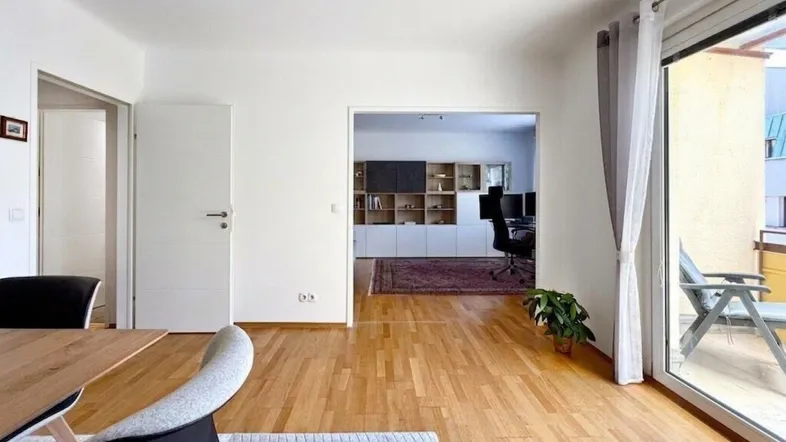 Heller Wohnbereich mit Holzboden und Zugang zu einem weiteren Zimmer sowie einem Balkon.