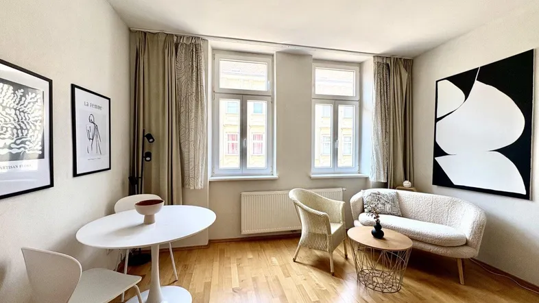 Helles Wohnzimmer mit Holzboden, gemütlicher Sitzecke und kleinem Essbereich, ideal für entspannte Stunden.