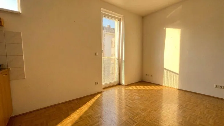 Helles Zimmer mit Parkettboden und Zugang zu einem Balkon, durchflutet von natürlichem Sonnenlicht.