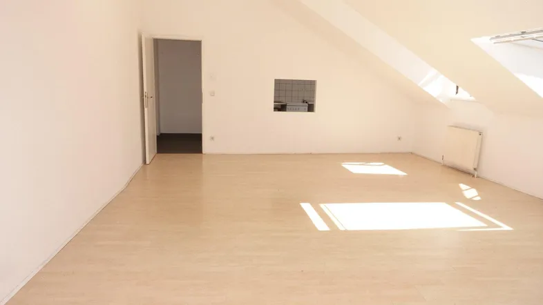 Heller Dachgeschossraum mit schrägen Wänden, Dachfenstern und hellem Laminatboden.