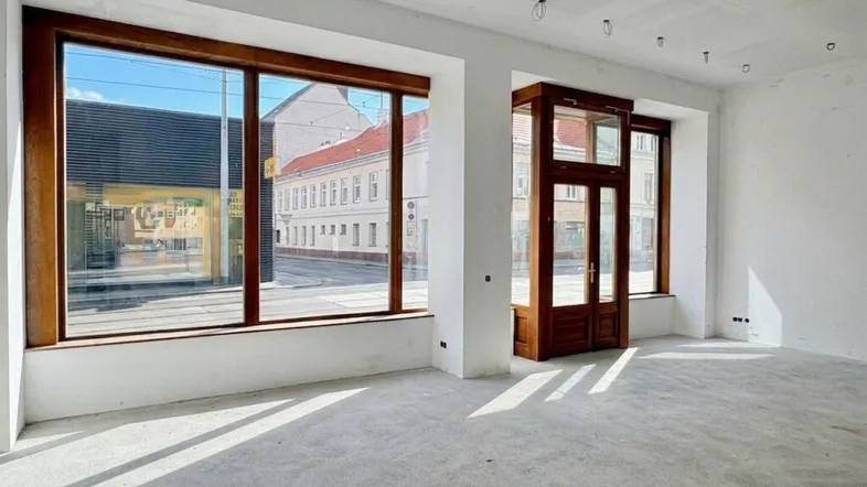 Heller, leerer Geschäftsraum mit großen Holzfenstern und Blick auf die Straße, bereit für den Ausbau.