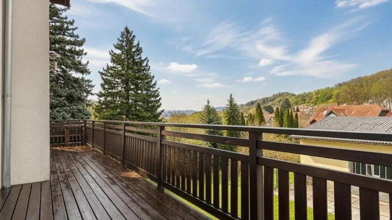 Geräumiger Holzbalkon mit dunklem Geländer und weitem Blick ins Grüne und auf die Umgebung.