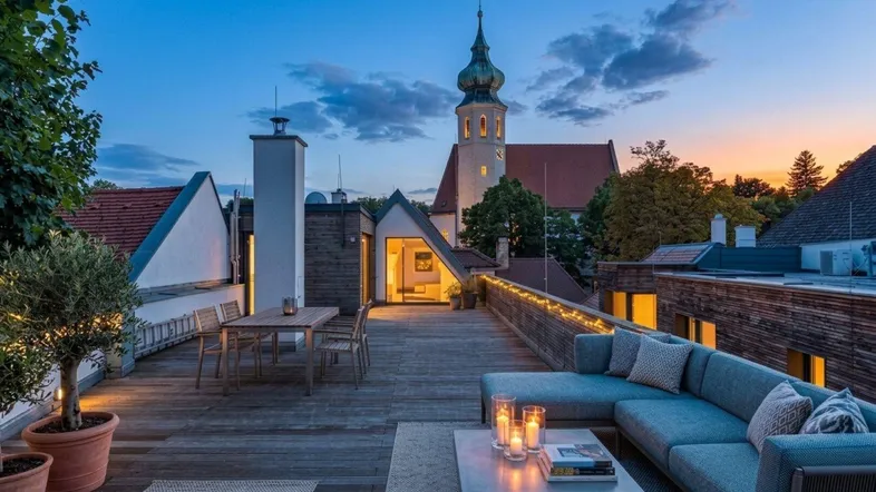 Geräumige Dachterrasse mit Lounge-Bereich, Esstisch und malerischem Blick auf die Kirche bei Sonnenuntergang.