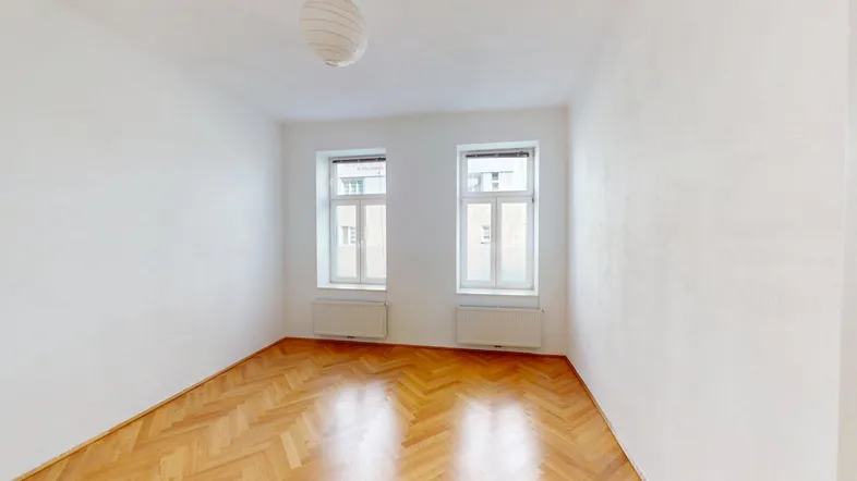 Helles Zimmer mit weiß gestrichenen Wänden und klassischem Fischgrätparkettboden.