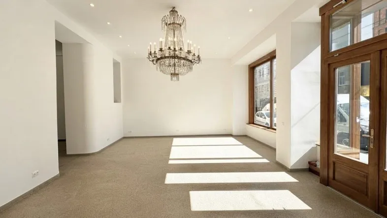 Geräumiger, heller Gewerberaum mit großen Fenstern, Holztüren und einem eleganten Kronleuchter.