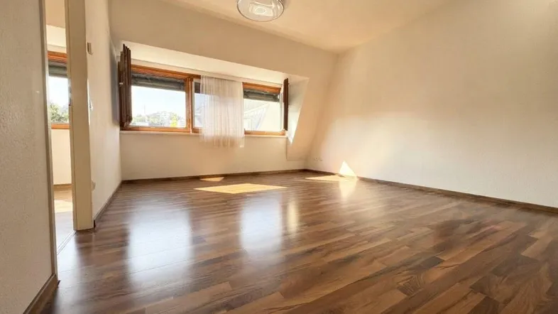 Helles Zimmer mit Holzboden und schrägen Wänden, ideal als Schlaf- oder Wohnbereich.