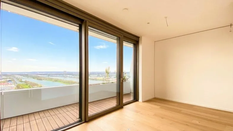 Helles Zimmer mit Holzboden und großen Schiebetüren, die zu einem Balkon mit weitem Blick führen.