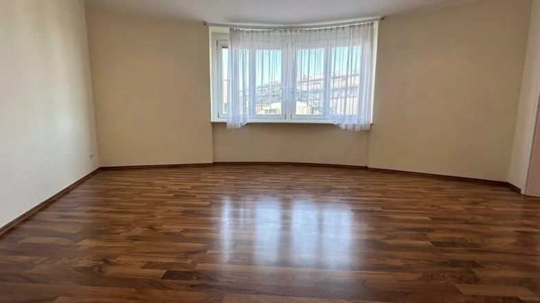Helles, leeres Zimmer mit Laminatboden und großen Fenstern, bereit zur individuellen Gestaltung.