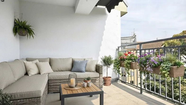Gemütlicher Balkon mit Rattan-Sofa, Markise und Blumenkästen, ideal für entspannte Stunden im Freien.