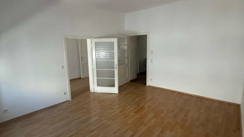 Helles, leeres Zimmer mit Laminatboden und Zugang zu weiteren Räumen.