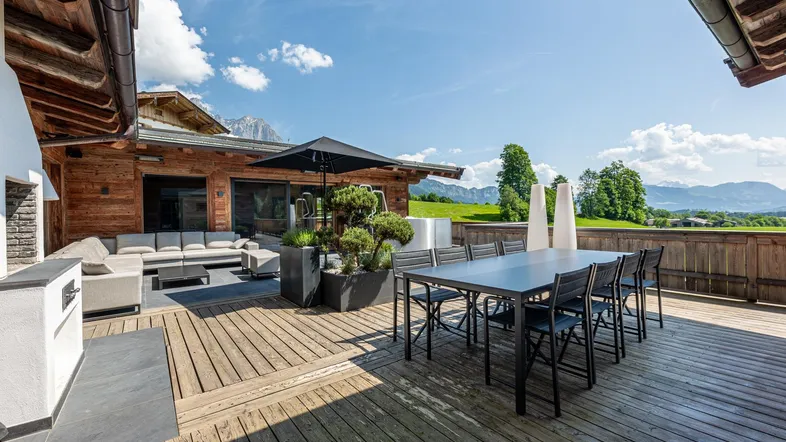 Geräumige Holzterrasse mit Essbereich, Lounge-Möbeln und weitem Blick auf die Berge und grüne Landschaft.