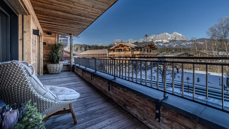Geräumiger Balkon mit Holzboden, gemütlichem Sessel und beeindruckendem Bergblick in sonniger Lage.