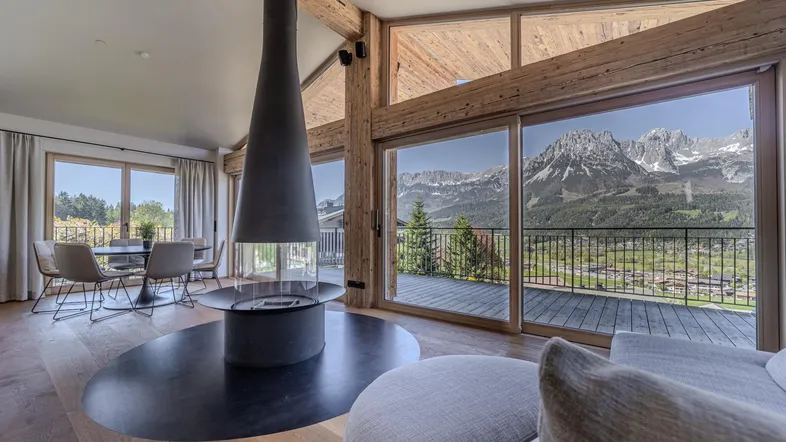 Geräumiger Wohn-Essbereich mit modernem Kamin, Holzbalken und Panoramafenstern mit Bergblick.