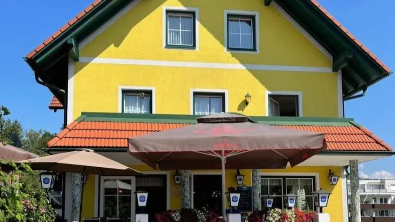 Gelbes Gebäude mit rotem Ziegeldach und einer einladenden Terrasse mit Sonnenschirmen und Blumenkästen.