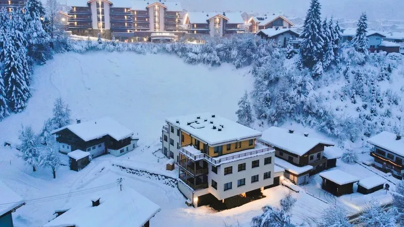 Winterliche Luftaufnahme eines Gebäudekomplexes in einer verschneiten Berglandschaft bei Dämmerung.