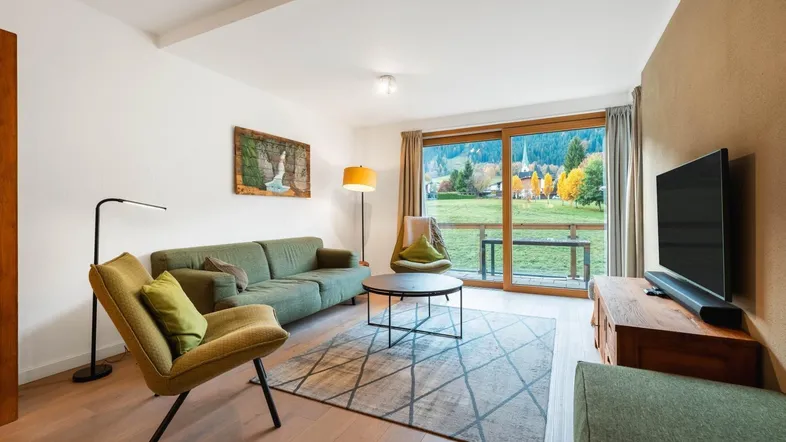 Helles Wohnzimmer mit gemütlichem Sofa, Holzboden und großem Fenster mit Bergblick.