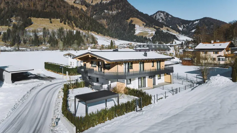 Modernes Haus in verschneiter Berglandschaft mit Holzelementen und Carport, umgeben von Natur.