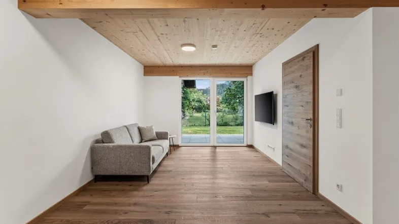 Helles Wohnzimmer mit Holzbalkendecke, Parkettboden und Zugang zur Terrasse.