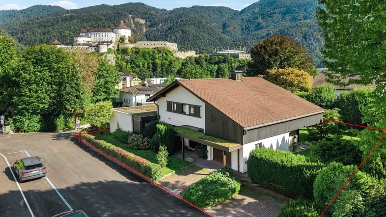 Luftaufnahme des Hauses mit Garten, umgeben von grünen Hügeln und einer Burg im Hintergrund.
