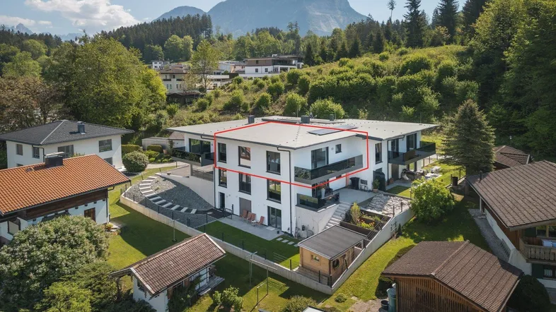 Moderne Wohnanlage in den Bergen mit Flachdach und Balkonen, umgeben von grüner Landschaft.