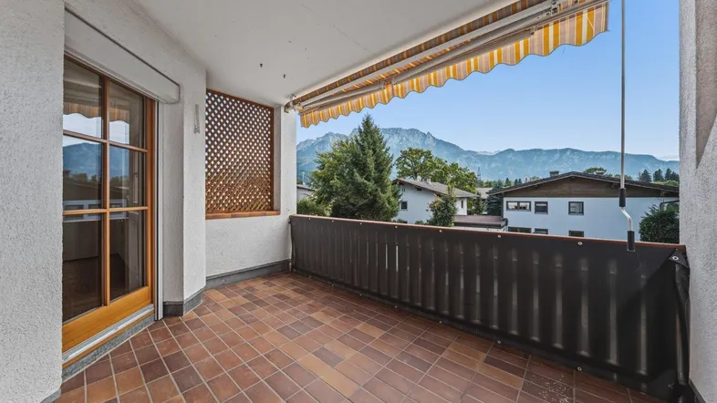Geräumiger Balkon mit Fliesenboden, Markise und malerischem Bergblick auf die Alpen.