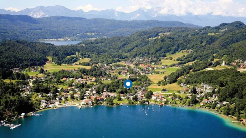 Panoramablick aus der Vogelperspektive auf ein Dorf am See mit umliegenden Bergen und Wäldern.