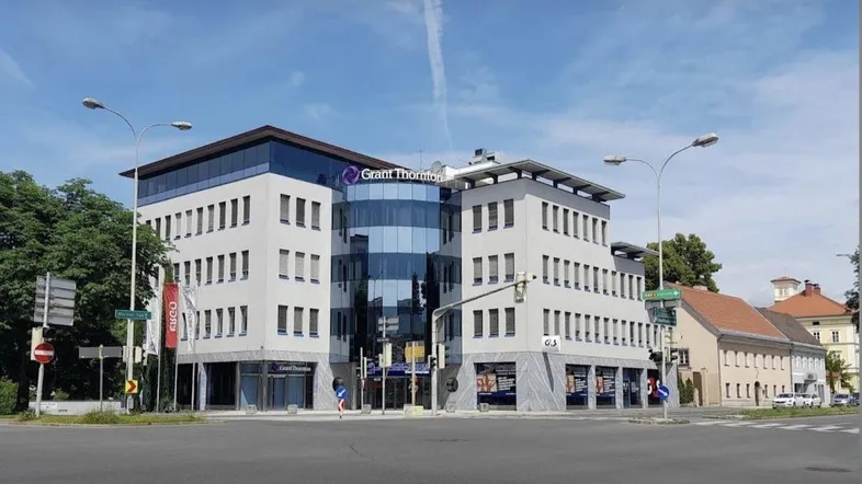 Modernes Bürogebäude mit Glasfassade an einer städtischen Kreuzung unter blauem Himmel.