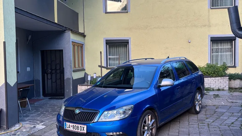 Blauer Kombi auf gepflastertem Hof vor einem gelben Wohngebäude.