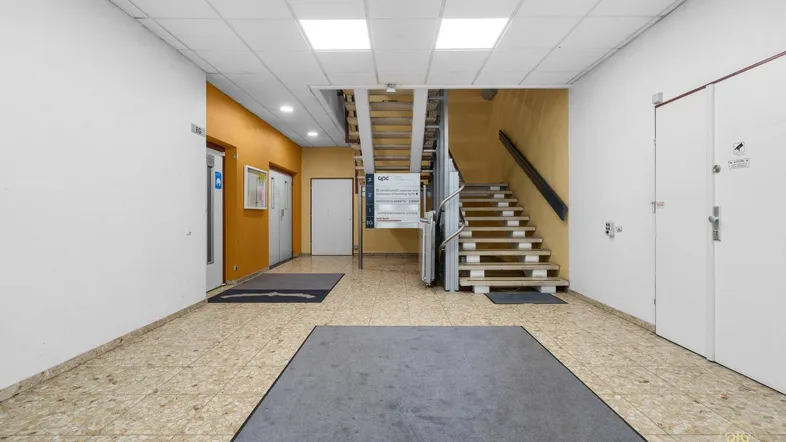 Heller Eingangsbereich mit Treppe, Aufzug und gefliestem Boden in einem Mehrfamilienhaus.