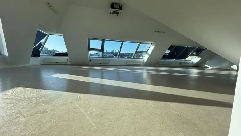 Großer, heller Raum im Dachgeschoss mit schrägen Wänden und großen Fenstern, ideal für Büro oder Studio.