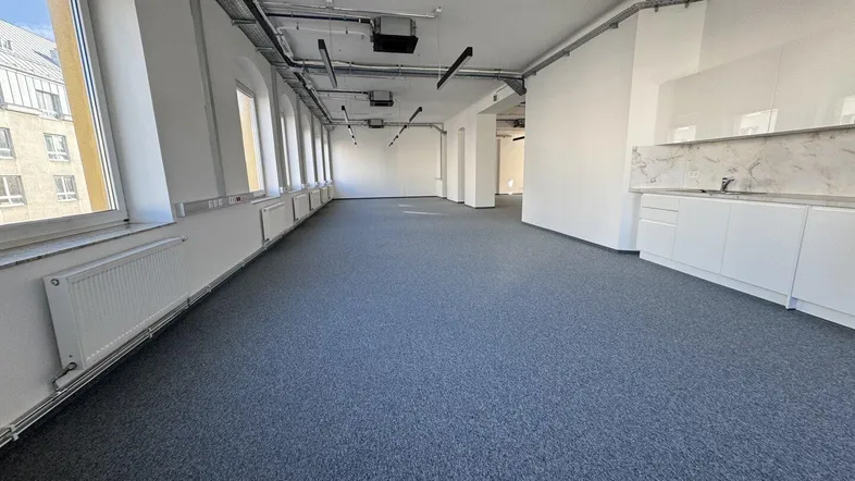 Großes, offenes Büro mit Teppichboden, vielen Fenstern und einer integrierten Küchenzeile für Mitarbeiter.